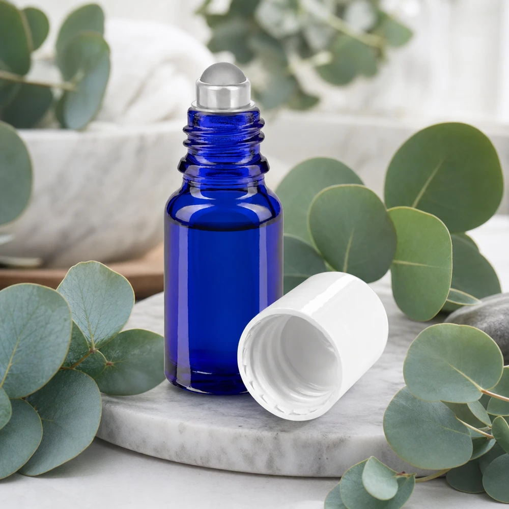 Flacon roll-on en verre d'apothicaire bleu cobalt de 10 ml, avec bille en acier inoxydable et bouchon blanc sur fond marbré