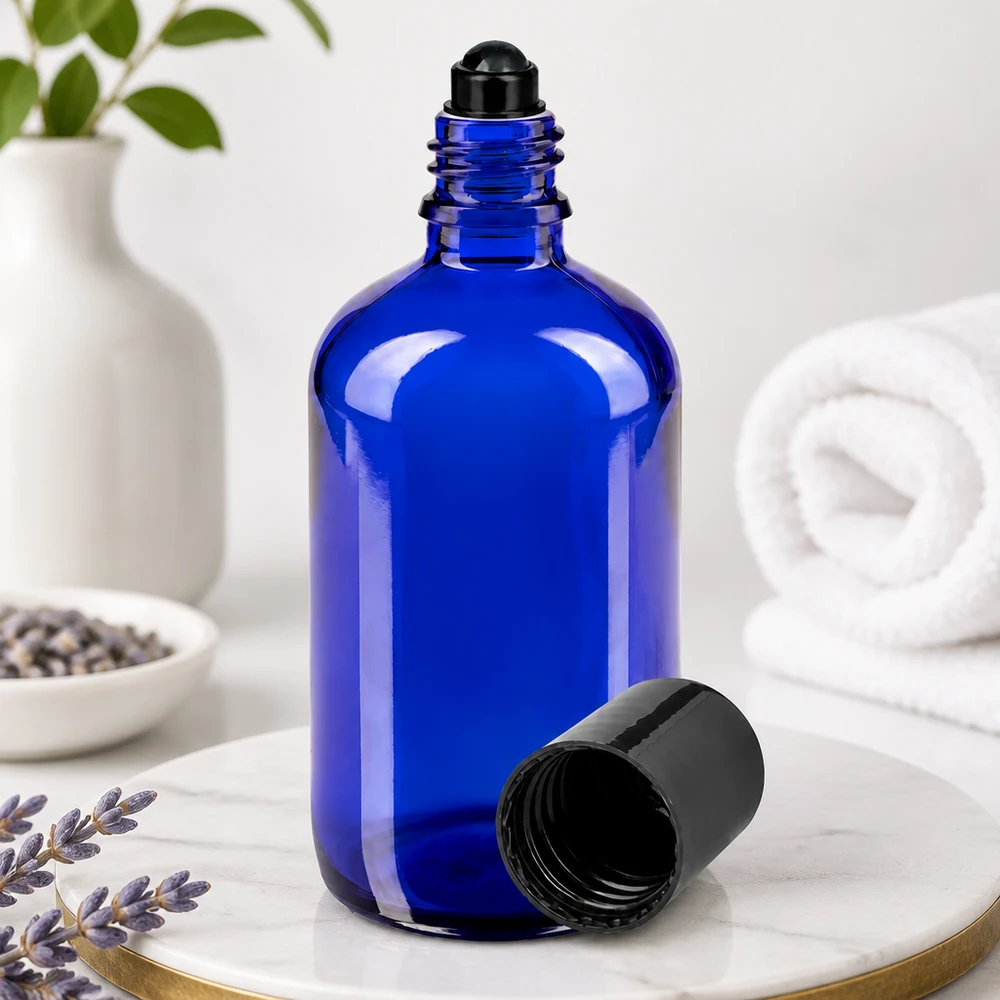 Flacon de déodorant en verre bleu 100 ml, déo à bille vide Flacon en verre bleu de 100 ml avec une bille roulante noire et le bouchon retiré, posé sur du marbre