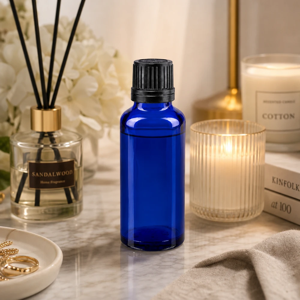 Flacon en verre bleu de 30 ml muni d'un bouchon compte-gouttes noir, posé sur du marbre à côté d'une bougie parfumée et d'un diffuseur d'ambiance