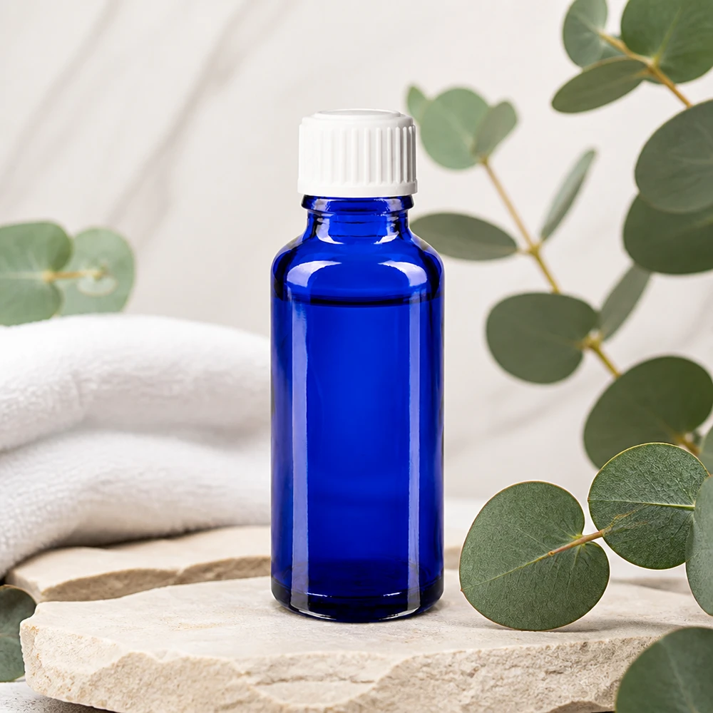 Flacon de pharmacie bleu cobalt de 30 ml avec bouchon compte-gouttes blanc, posé sur une pierre naturelle parfumée à l'eucalyptus