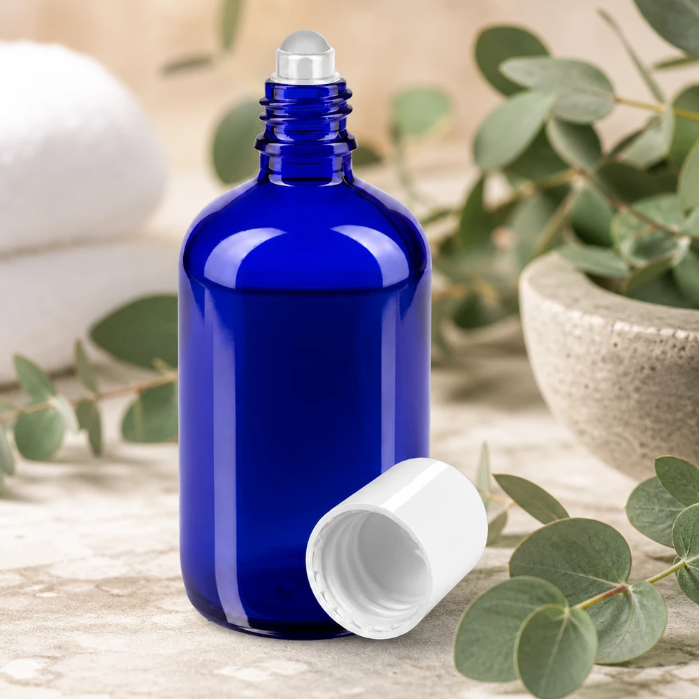 Flacon roll-on bleu de 100 ml, muni d'une bille en acier et d'un bouchon blanc, posé parmi des branches d'eucalyptus