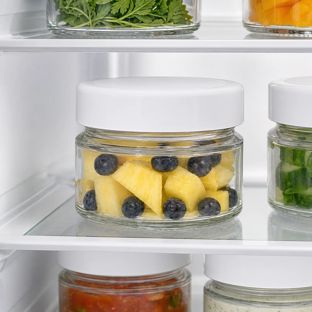 Un bocal rond de 80 ml au réfrigérateur contenant de l'ananas et des myrtilles montre les propriétés de conservation optimales du couvercle BasicSeal