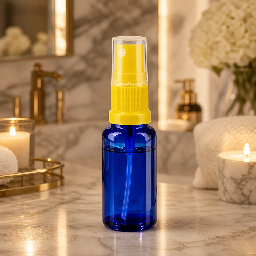 Flacon vaporisateur en verre bleu de 20 ml avec tête de pulvérisation jaune, posé sur une étagère de salle de bains en marbre