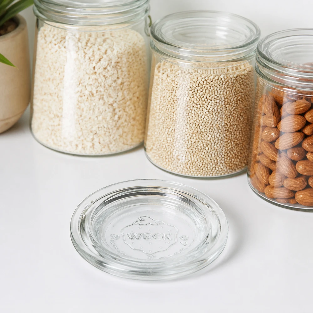 WECK Couvercle en verre RR40 transparent devant des bocaux de stockage avec riz Quinoa et noix sur un plan de travail blanc