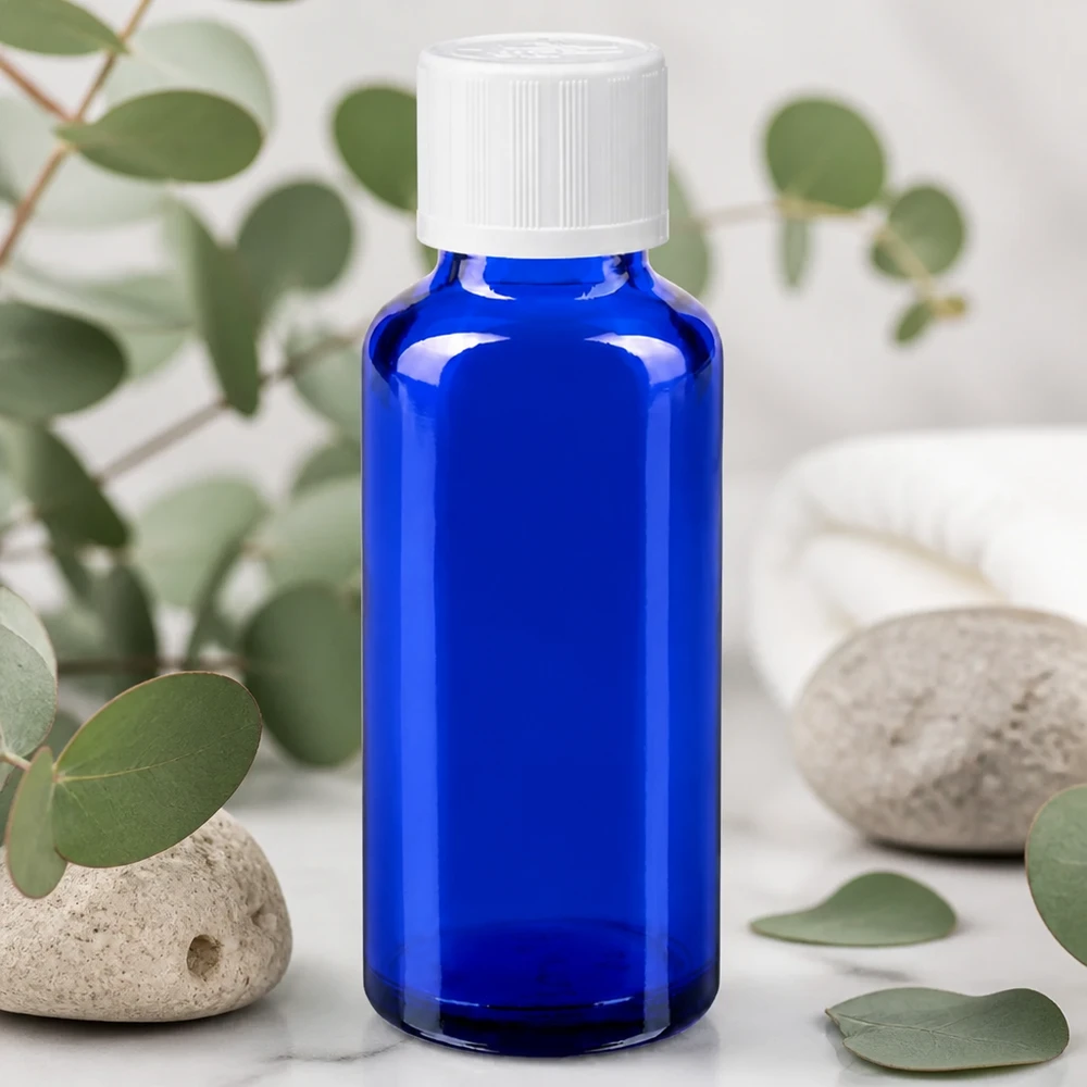 Flacon à pharmacie bleu 30ml bouchon anti-goutte blanc séc. enf. std Flacon de pharmacie bleu cobalt de 30 ml muni d'un bouchon KiSi blanc, posé sur du marbre au milieu de branches d'eucalyptus