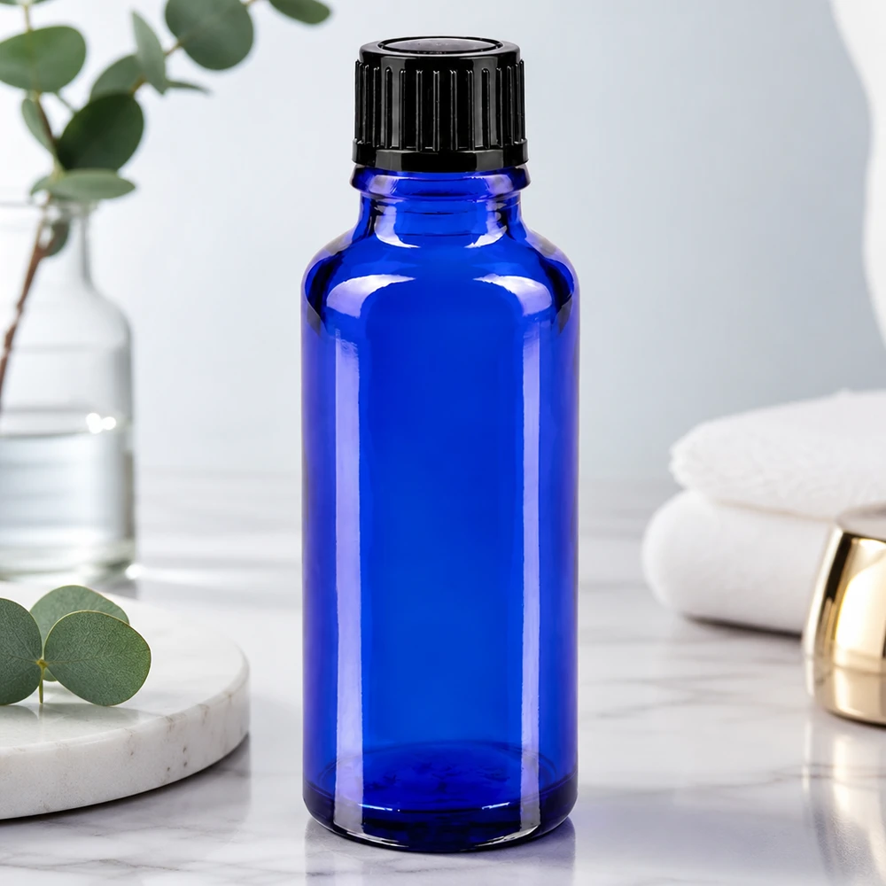 Flacon en verre bleu cobalt de 30 ml avec bouchon à vis noir, posé sur une surface en marbre blanc