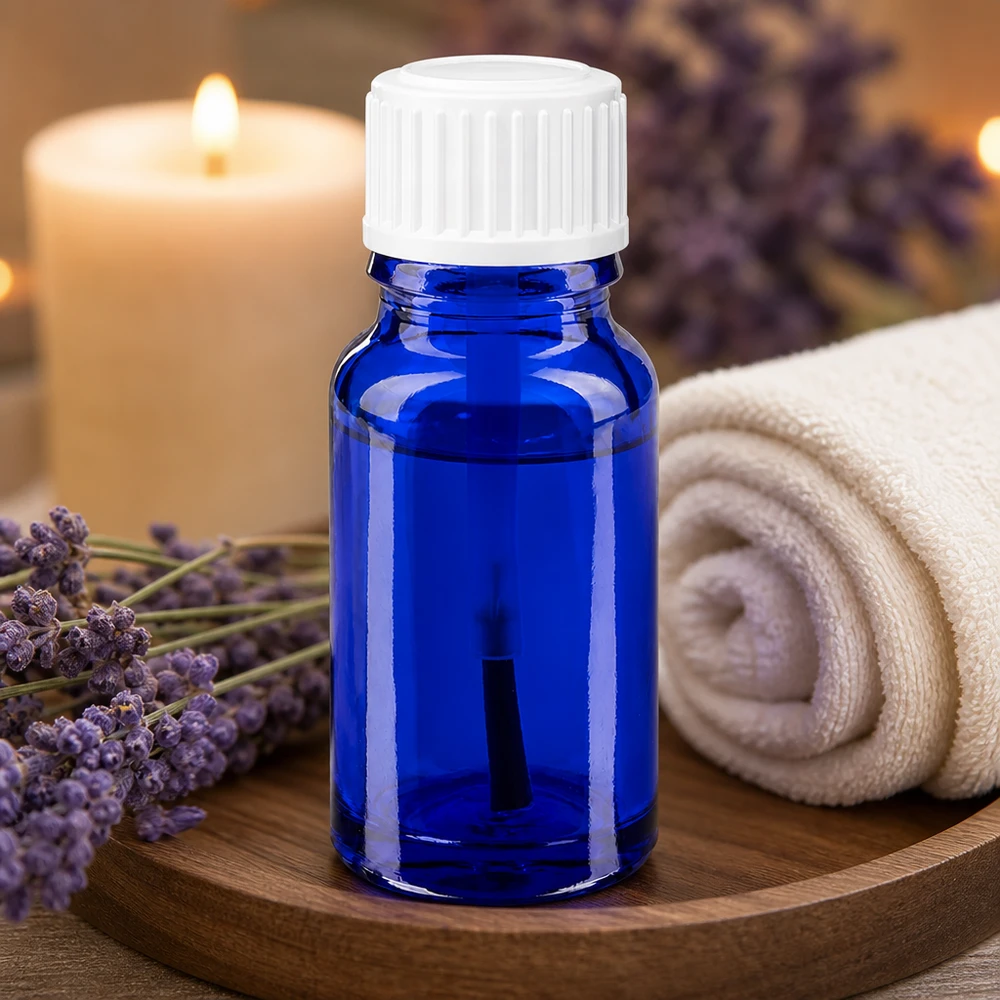 Flacon d'aromathérapie de 10 ml en verre d'apothicaire bleu, muni d'un embout pinceau blanc, à côté de fleurs de lavande