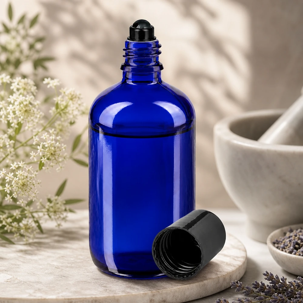 Flacon en verre bleu cobalt de 100 ml avec bille roulante noire, ouvert, posé à côté de fleurs de lavande et d'un mortier