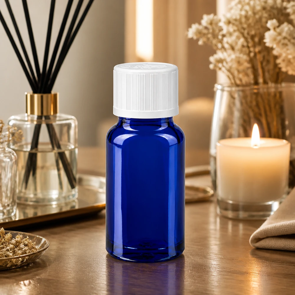 Petite bouteille en verre bleue de 10 ml avec un bouchon à vis blanc, posée sur une table en bois à côté d'un diffuseur de parfum d'ambiance et d'une bougie
