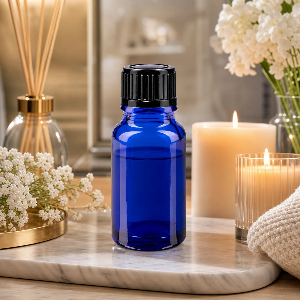 Flacon de pharmacie bleu 10ml, noir 1mm std Petite bouteille en verre bleue de 10 ml avec un bouchon noir, posée sur un plateau en marbre à côté de bougies