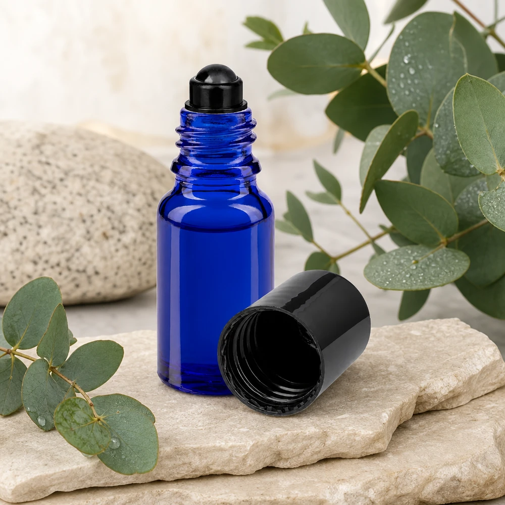 Flacon de déodorant en verre bleu 10 ml, déo à bille vide Flacon roll-on ApoGlas bleu de 10 ml avec bouchon noir, posé à côté de branches d'eucalyptus sur une pierre naturelle