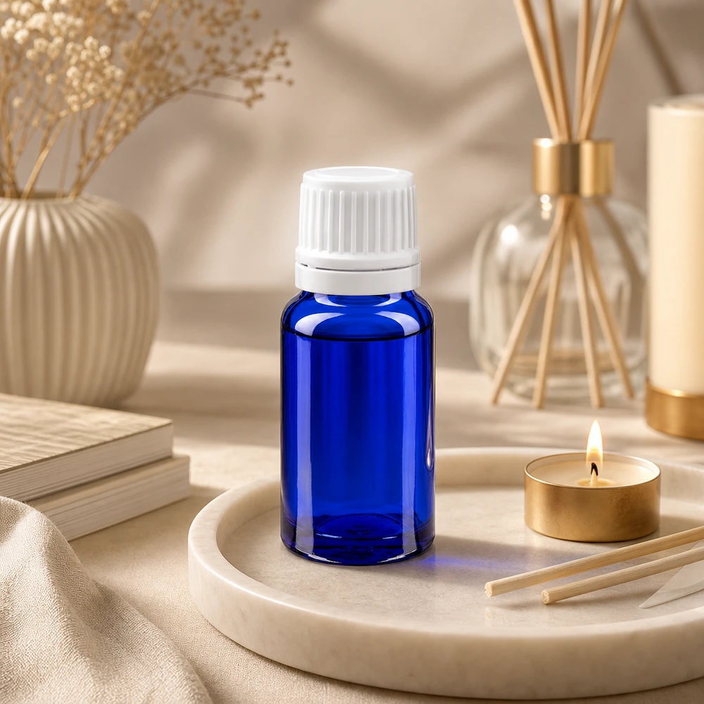 Flacon de pharmacie bleu 10ml bouchon inviolabilité blanc 1.2mm Petite bouteille en verre bleue avec un bouchon à vis blanc, posée sur un plateau en marbre à côté d'une bougie chauffe-plat
