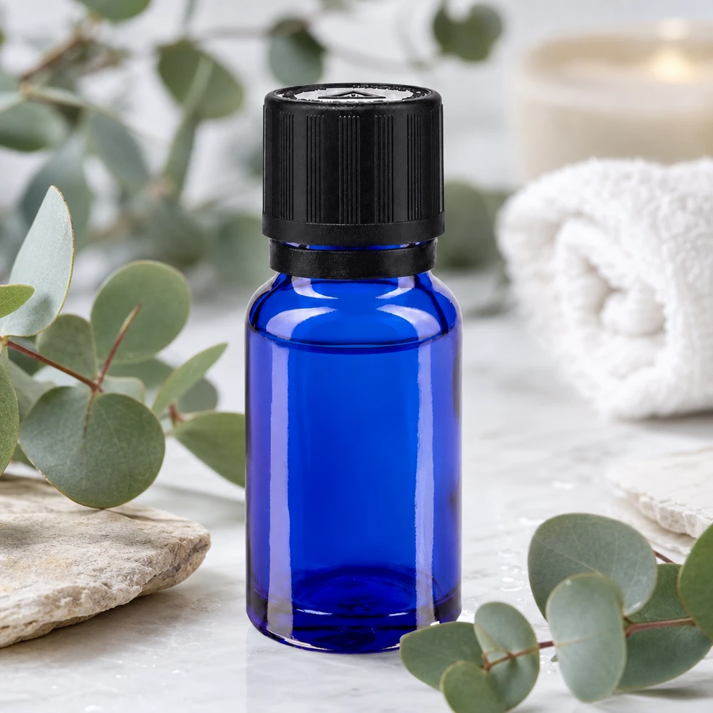 Flacon de pharmacie bleu 10ml bouchon inviolable blanc 1mm,séc. enf. bouchon inviolabilité Flacon de pharmacie bleu cobalt de 10 ml muni d'un bouchon OV noir, posé sur du marbre au milieu de branches d'eucalyptus