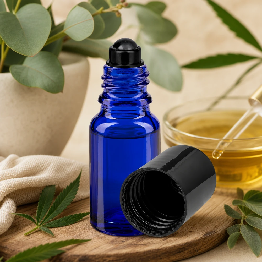 Flacon de déodorant en verre bleu 10 ml, déo à bille vide Flacon roll-on ApoGlas bleu de 10 ml avec bouchon noir, posé sur une planche en bois à côté d'une feuille de cannabis et d'un eucalyptus
