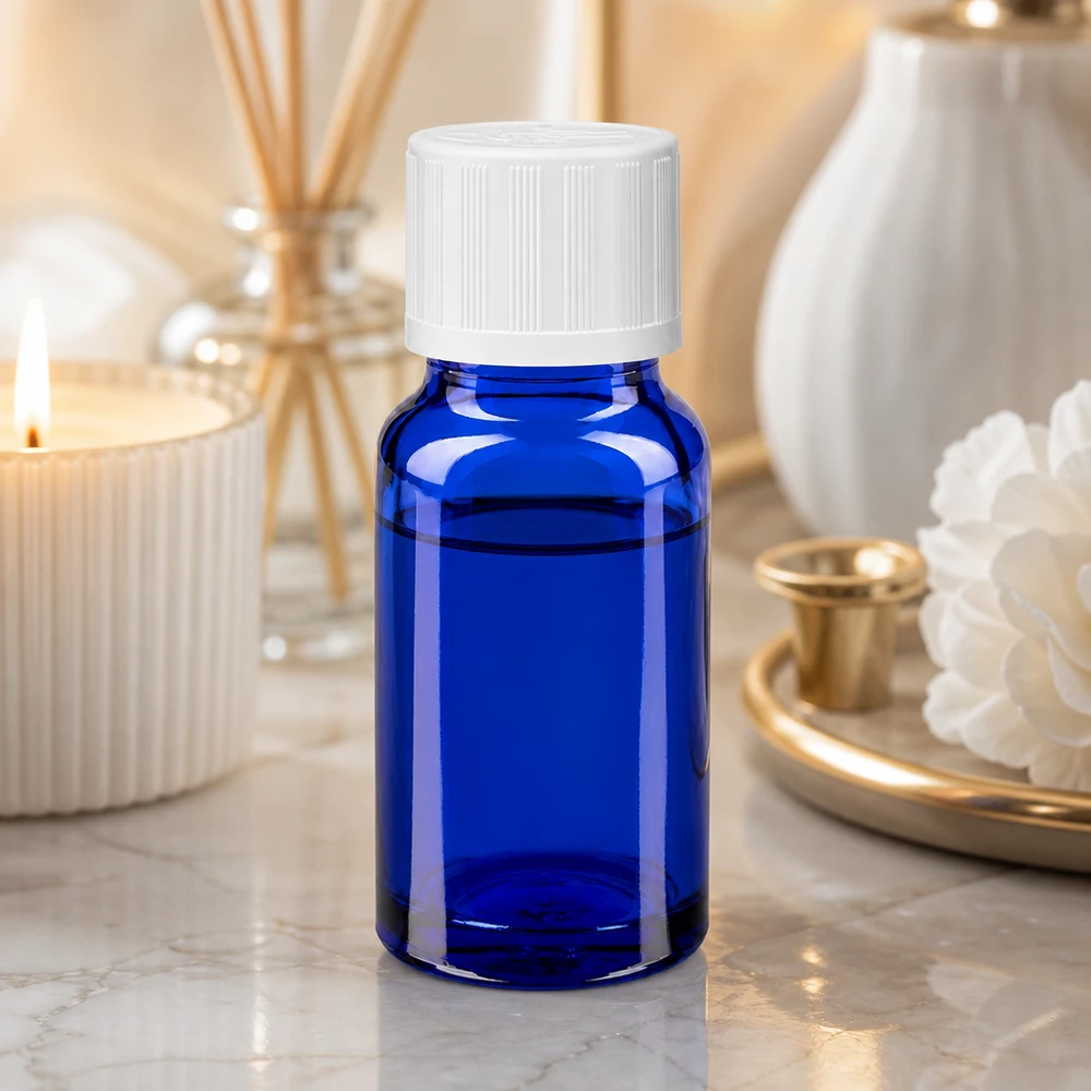 Petite bouteille en verre bleue avec un bouchon à vis blanc, posée sur une surface en marbre à côté d'une bougie et d'un diffuseur