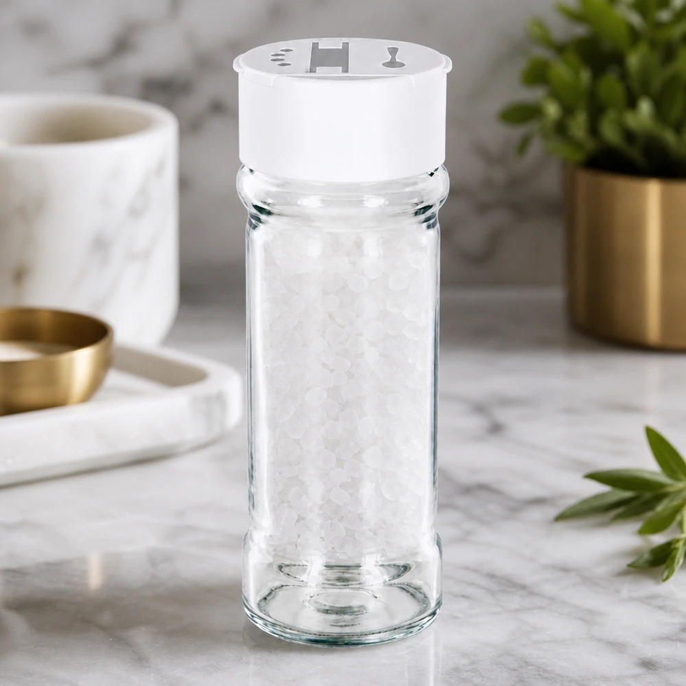Pot à sel/épices 100 ml avec double saupoudreuse, blanc Pot à épices transparent de 100 ml avec saupoudreuse double blanche posée sur du marbre, rempli de gros sel marin