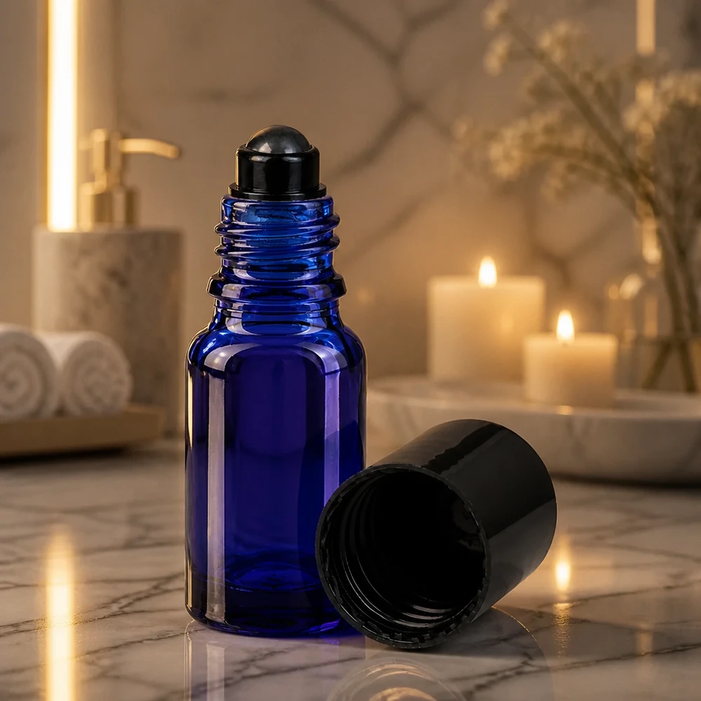 Flacon roll-on bleu cobalt de 10 ml avec bille noire, sous la lumière tamisée d'une bougie posée sur du marbre