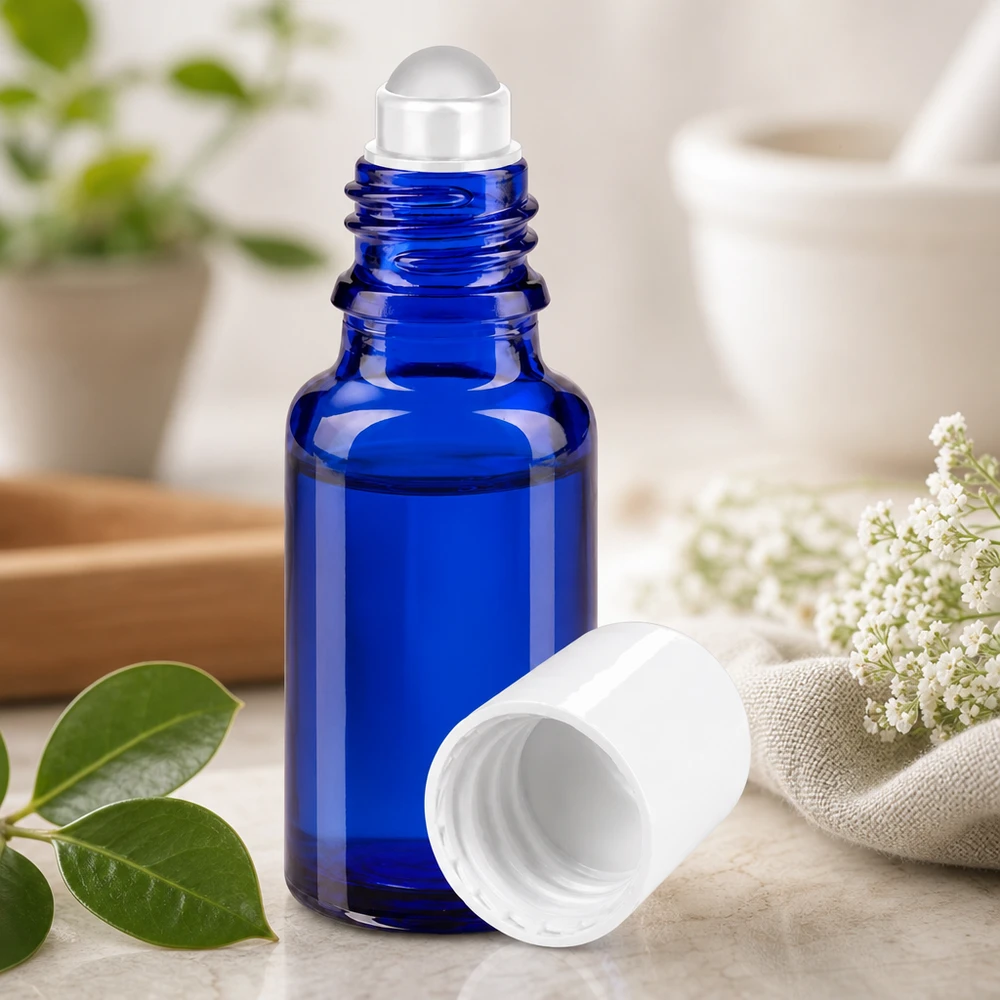 Flacon en verre de pharmacie bleu de 20 ml muni d'une bille roulante transparente, à côté de fleurs blanches et de feuilles vertes