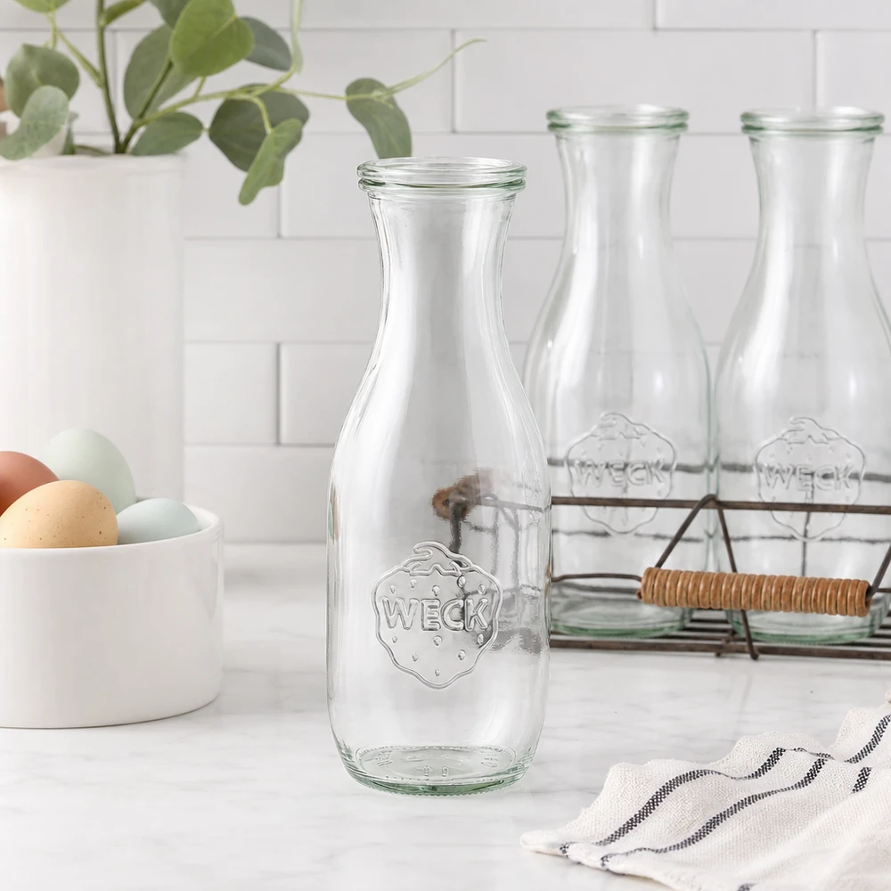 Bouteille à jus de 1 062 ml avec couvercle en verre WECK RR60 WECK Bouteille de jus de fruit 1062ml Bouteille en verre vide dans une cuisine blanche moderne avec coquille d'oeuf panier en fil métallique et plante