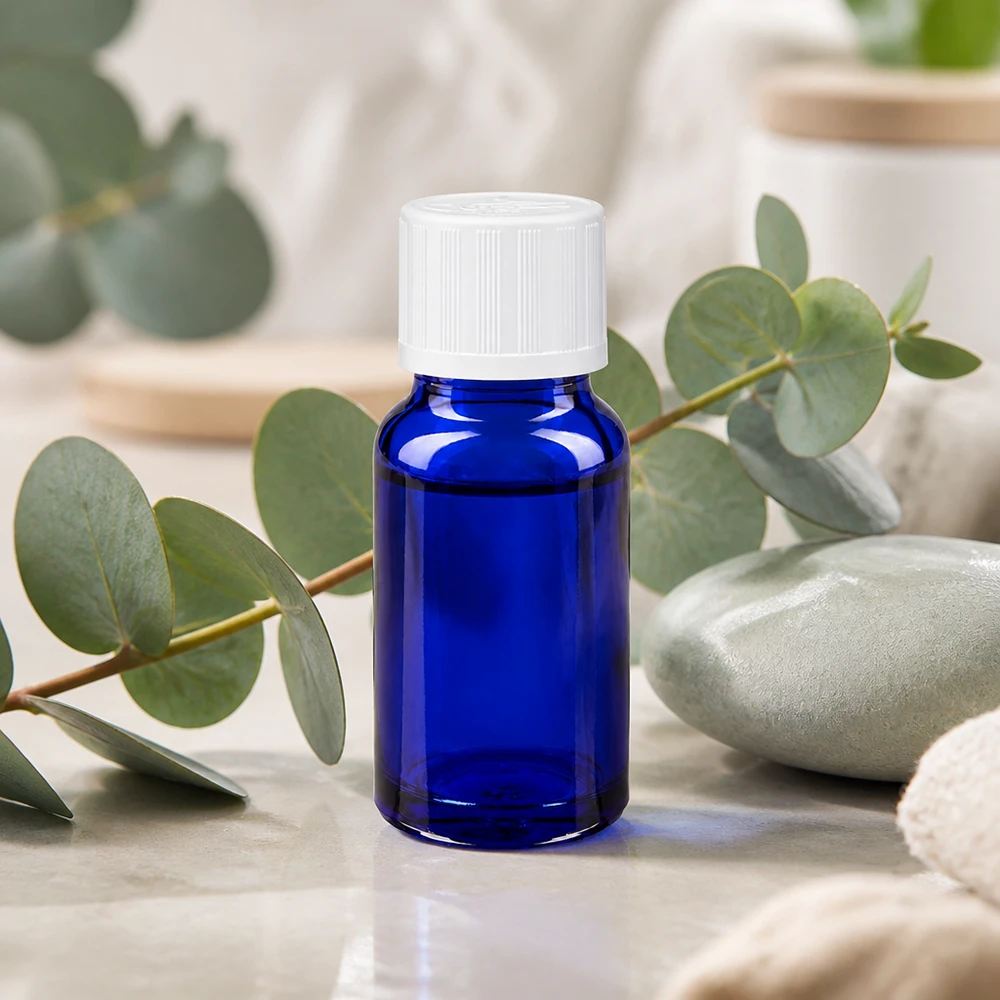 Flacon de pharmacie bleu cobalt de 10 ml muni d'un bouchon KiSi blanc, posé devant des branches d'eucalyptus sur du marbre
