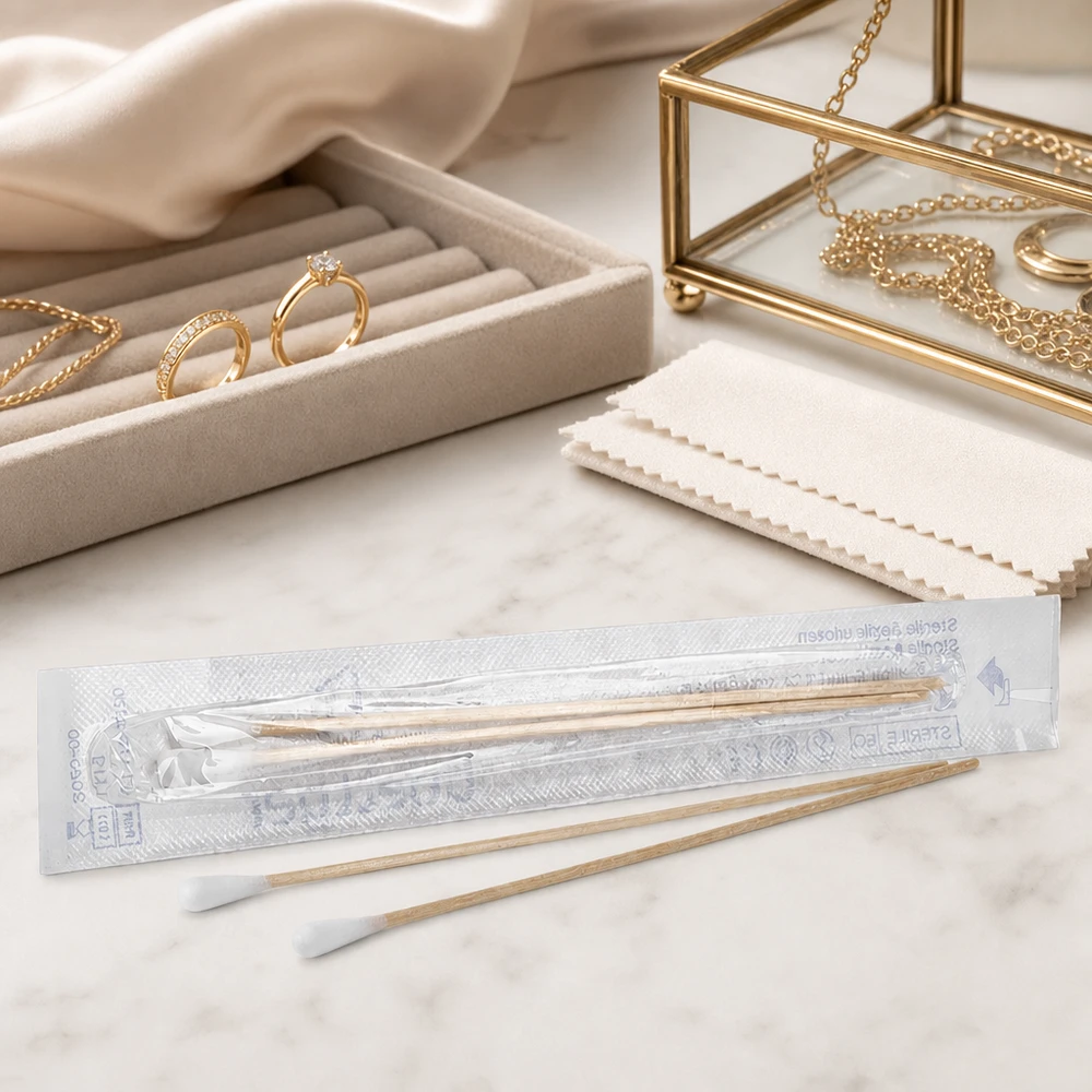 Écouvillon STÉRILE Lot de 2 cotons-tiges stériles dans un emballage transparent, à côté d'un coffret à bijoux et de bagues en or posés sur du marbre