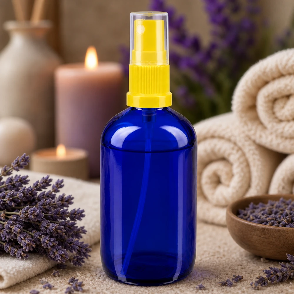Petit flacon en verre bleu de 100 ml muni d'un vaporisateur jaune, entouré de lavande et de bougies