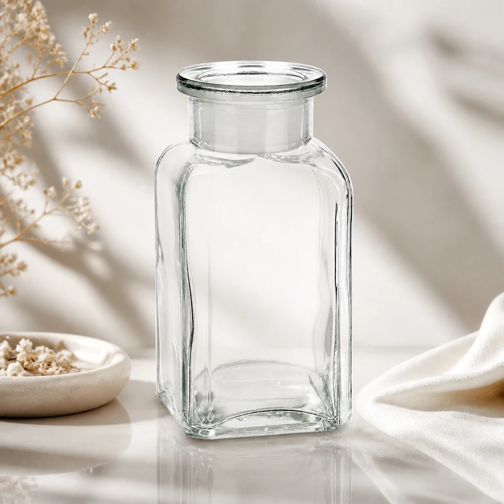 Bouteille carrée transparente vide de 100 ml à col large, posée sur un élégant tissu blanc et des fleurs séchées