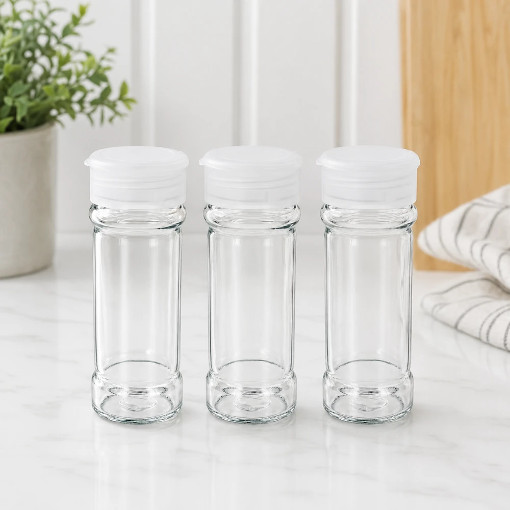 Pot à sel/épices 100 ml avec saupoudreuse, blanc Trois bocaux à épices en verre transparent vides de 100 ml avec des couvercles saupoudreurs blancs, posés sur une surface en marbre