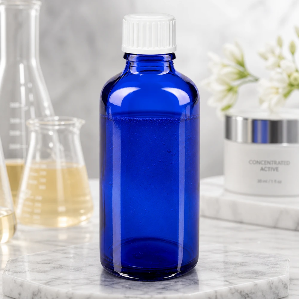Flacon en verre bleu cobalt de 50 ml avec bouchon à vis blanc, à côté d'un ballon de laboratoire et d'une crème de soin pour la peau