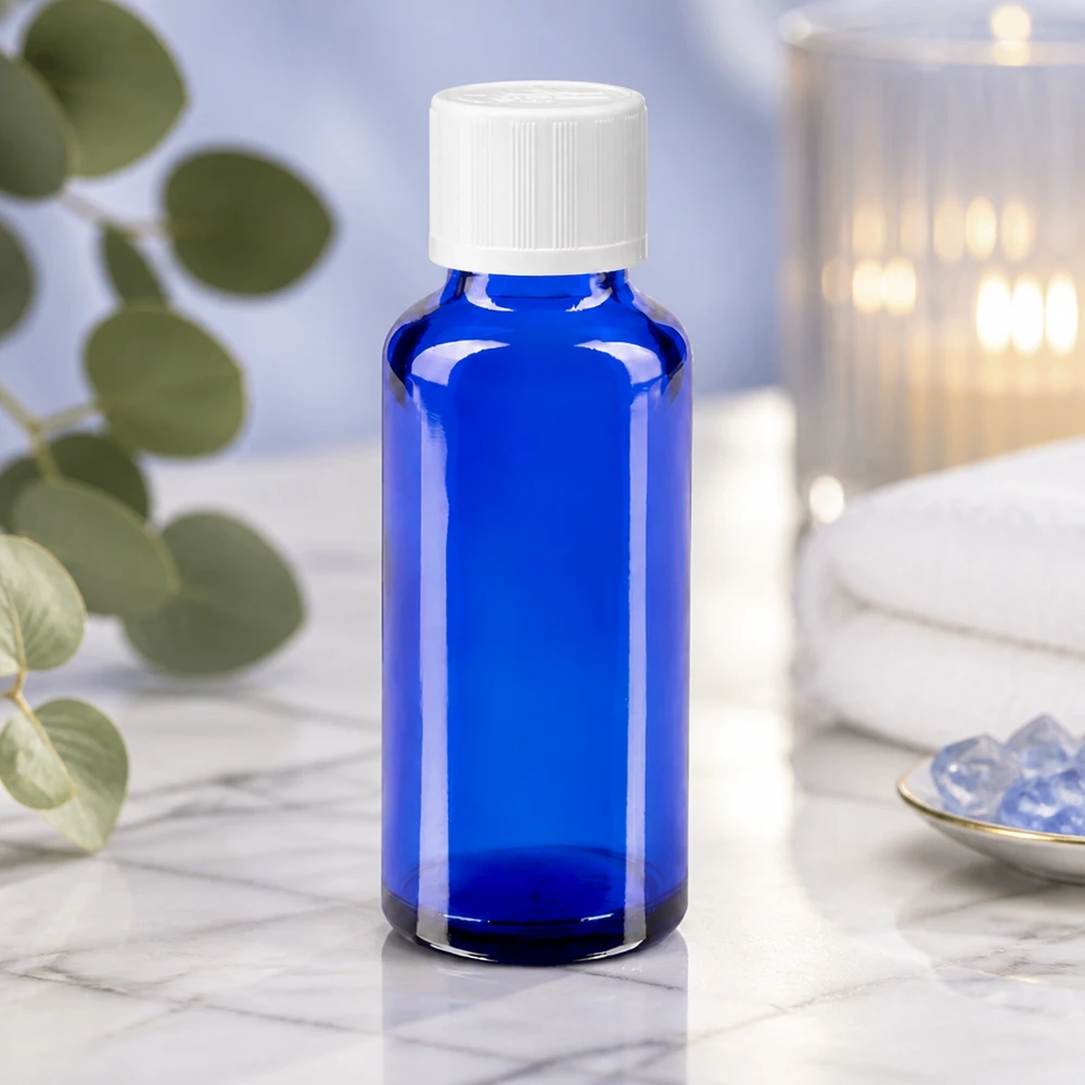 Flacon à pharmacie bleu 30ml bouchon anti-goutte blanc séc. enf. std Flacon de pharmacie bleu de 30 ml avec bouchon à vis blanc, posé sur du marbre blanc à côté de cristaux et d'une bougie