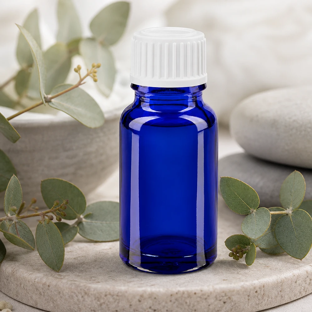 Flacon de pharmacie bleu 10ml bouchon vissable blanc globuli std Flacon en verre bleu cobalt de 10 ml muni d'un bouchon blanc standard, posé parmi des branches d'eucalyptus
