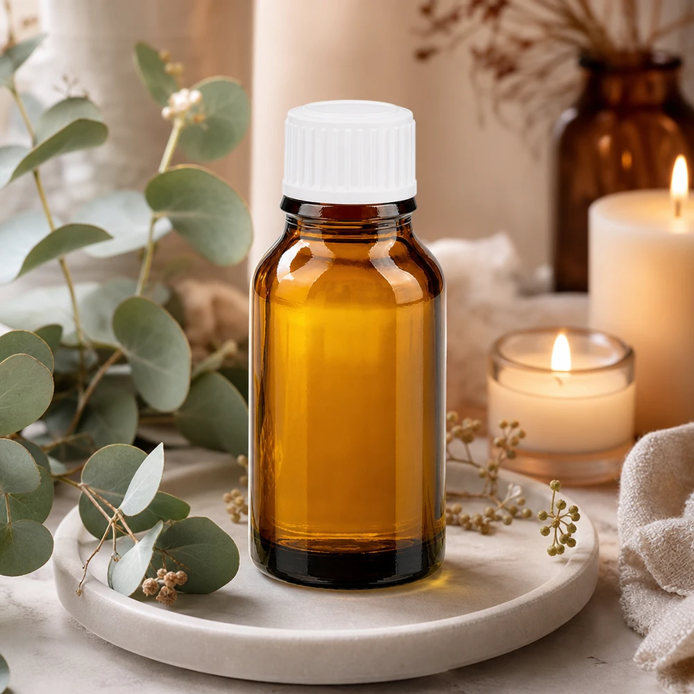 Petite bouteille en verre de 15 ml, de couleur marron, avec un bouchon à vis blanc, posée sur un plateau en marbre orné d'eucalyptus