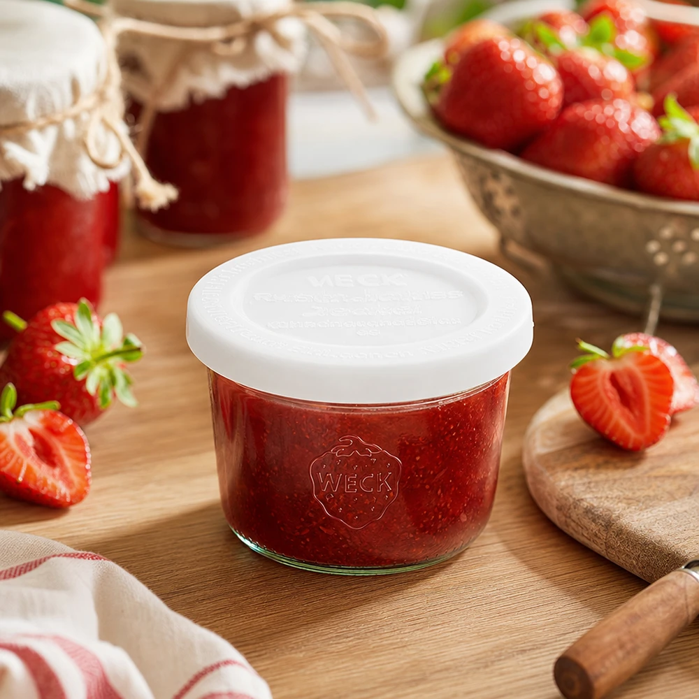 Bocal en verre de 80 ml avec couvercle hermétique WECK RR60 WECK Pot renversé de 80ml RR60 rempli de confiture de fraises sur planche en bois entourée de fraises fraîches et de pots de confiture