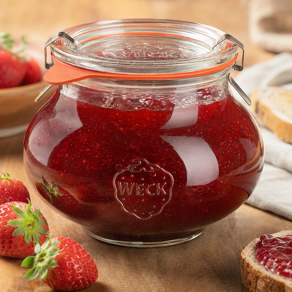 Bocal décoratif WECK RR80 de 560 ml, complet WECK Pot à bijoux 560ml rempli de confiture de fraises maison, fermeture à étrier fermée, entouré d'œufs frais.