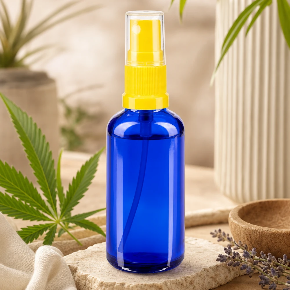 Flacon de pharmacie bleu 50ml embout spray jaune Flacon pulvérisateur STD bleu de 50 ml en verre de pharmacie, muni d'un pulvérisateur jaune, à côté d'une feuille de cannabis