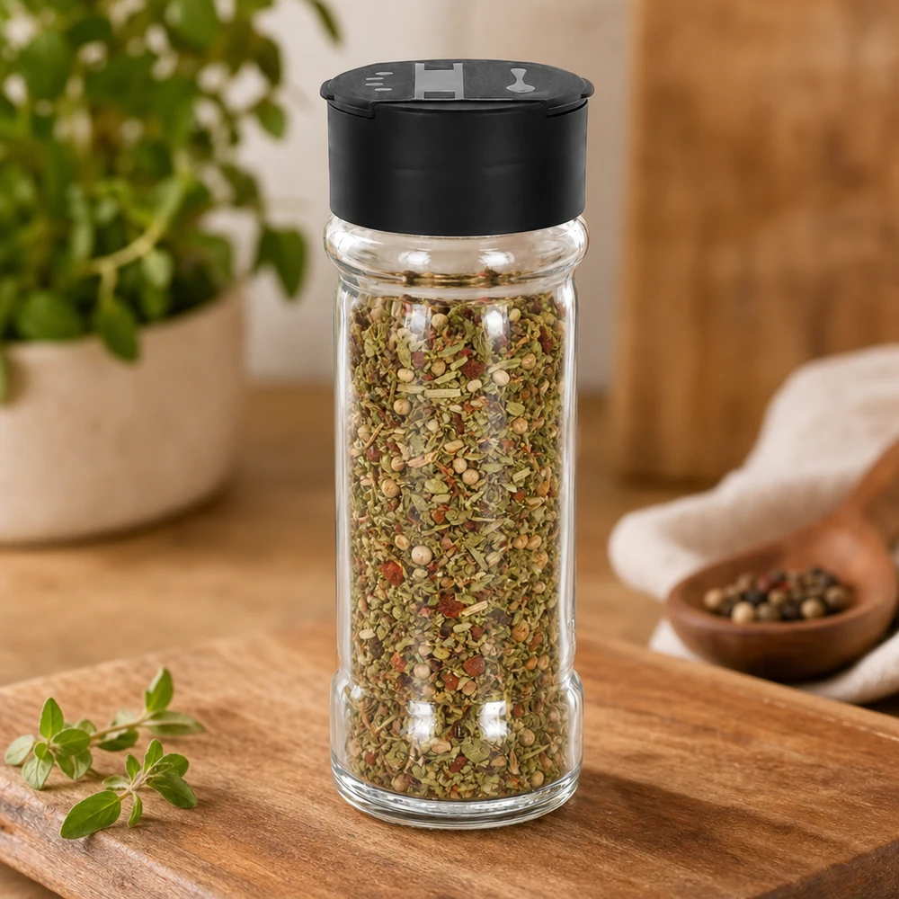 Mélange d'herbes dans un saupoudreur en verre transparent de 100 ml avec un couvercle noir à double saupoudreur, posé sur une planche en bois