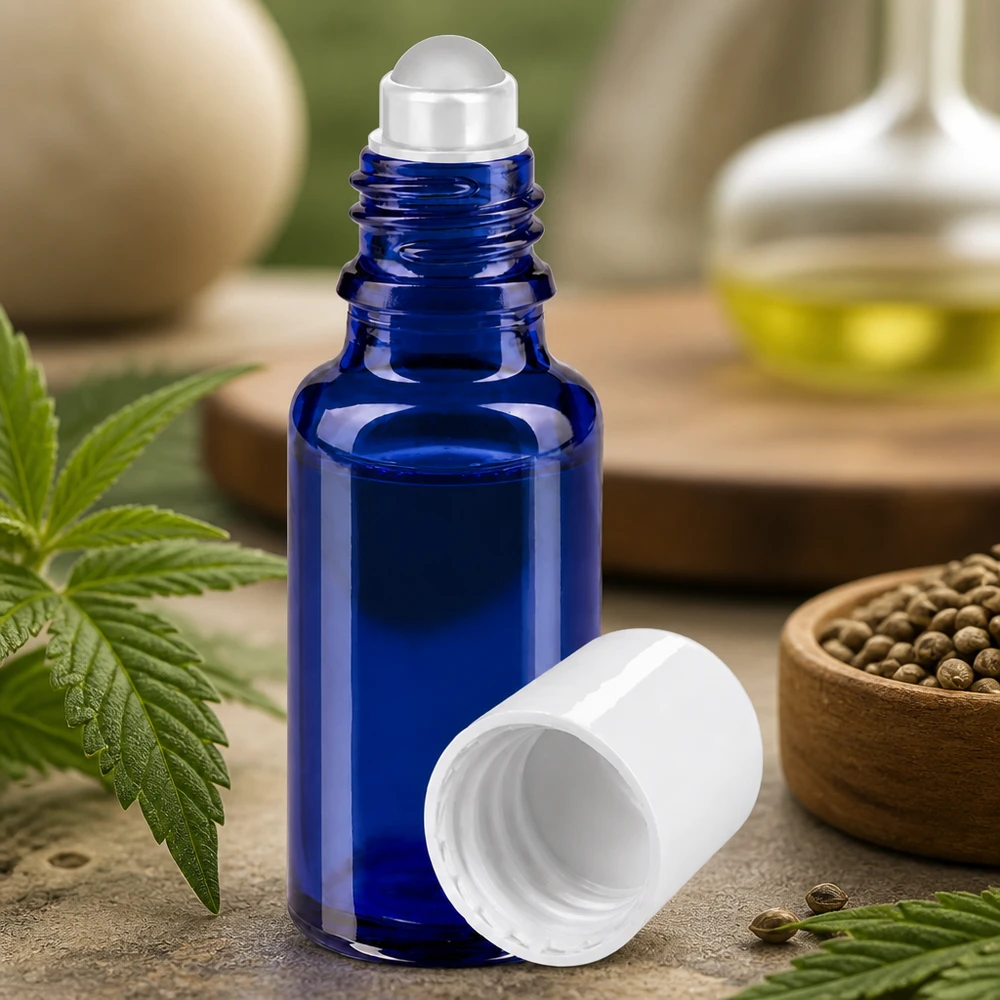 Flacon en verre bleu de 20 ml muni d'un applicateur à bille et d'un bouchon blanc, entouré de feuilles et de graines de chanvre