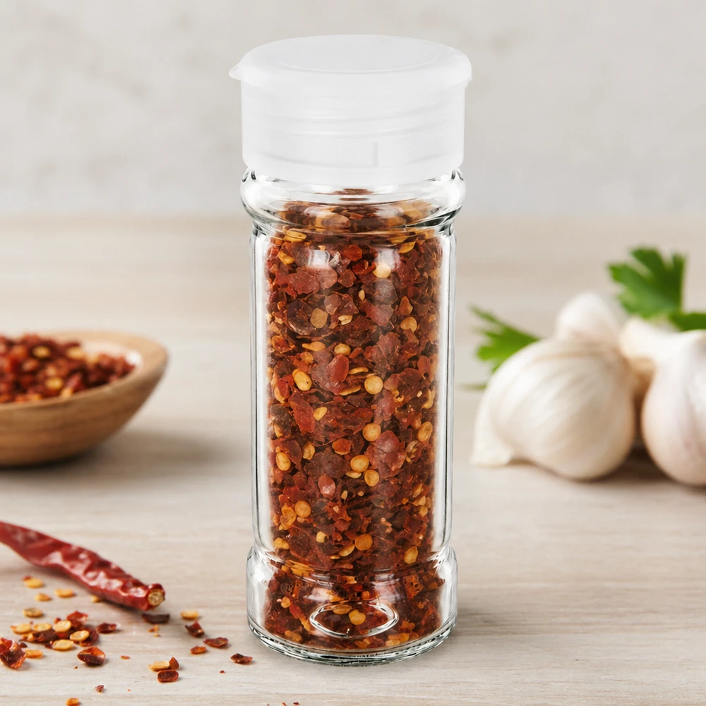 Pot à sel/épices 100 ml avec saupoudreuse, blanc Petit pot à épices de 100 ml muni d'un saupoudreur blanc, rempli de flocons de piment rouge, avec de l'ail en arrière-plan