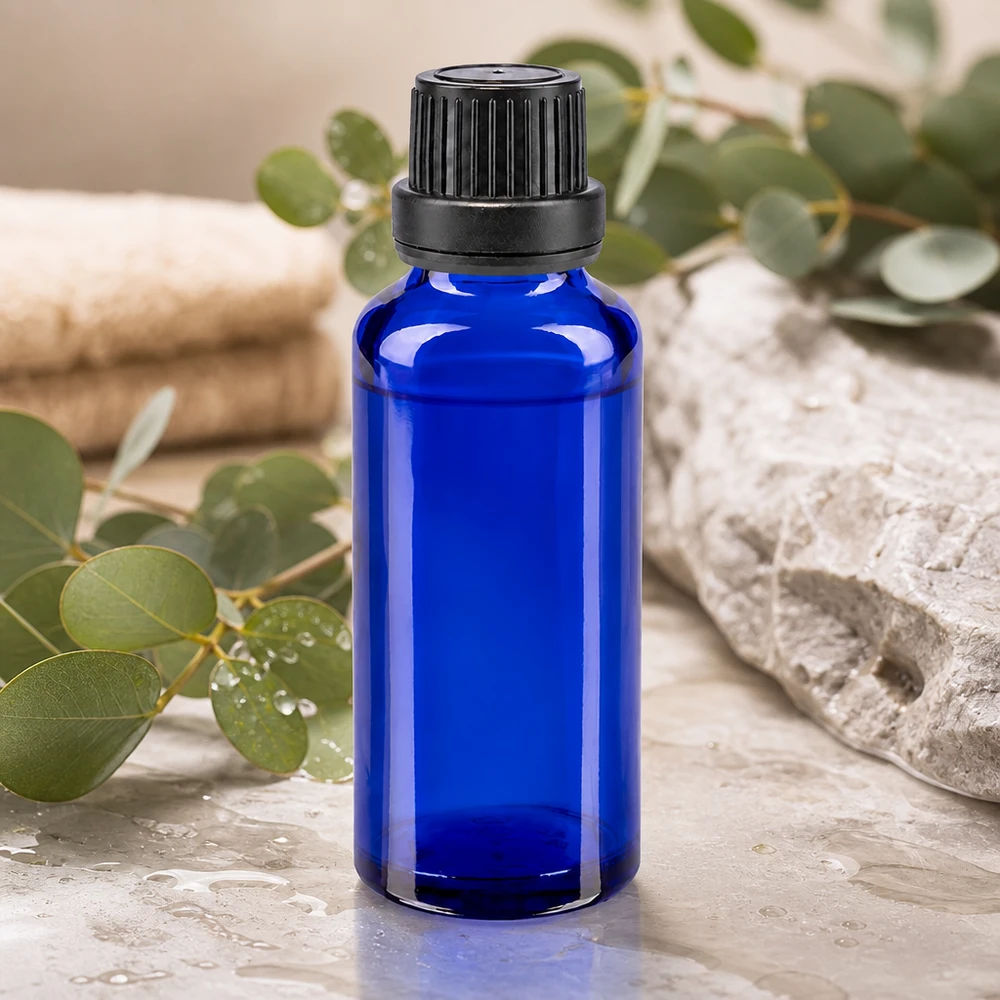 Flacon de pharmacie bleu cobalt de 30 ml avec bouchon OV noir, posé sur une pierre naturelle et orné de brindilles d'eucalyptus