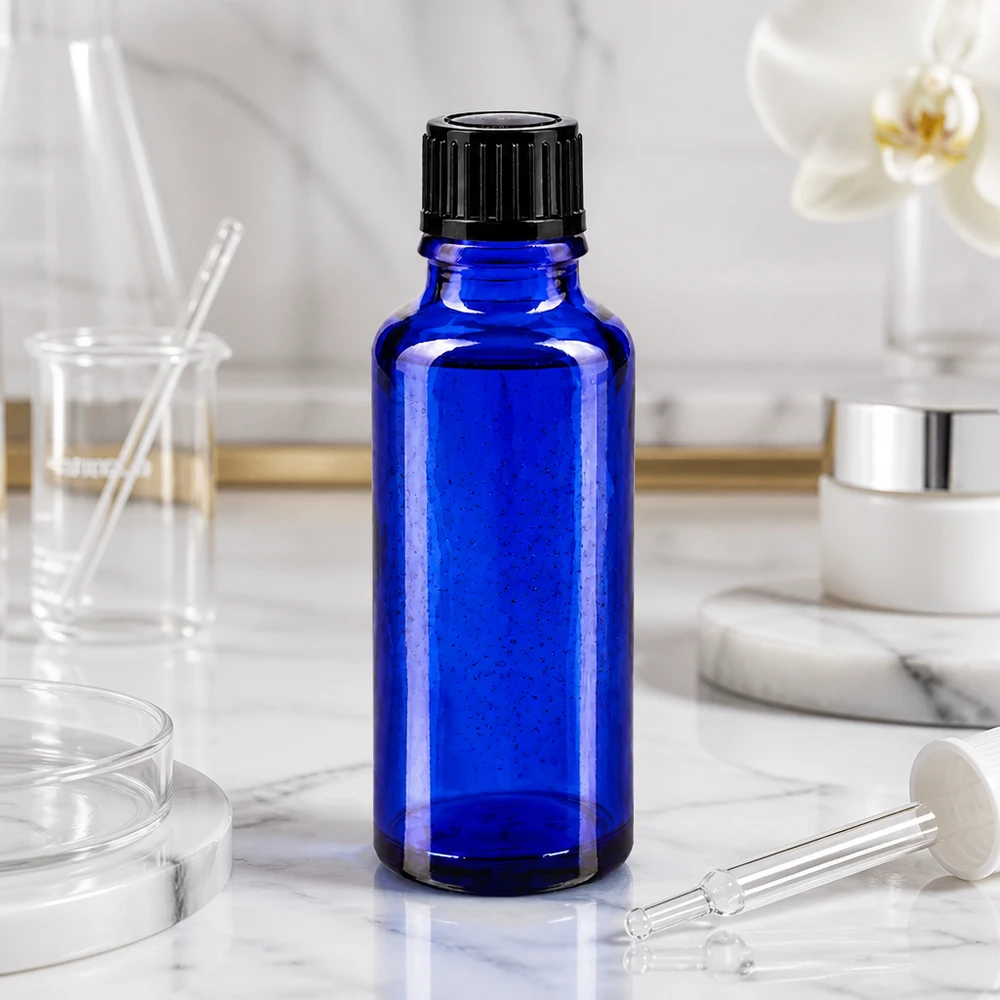 Flacon en verre bleu cobalt de 30 ml avec bouchon à vis noir, posé sur du marbre blanc