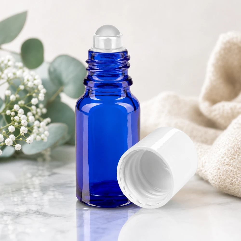Flacon roll-on en verre d'apothicaire bleu cobalt de 10 ml avec bille en verre transparente posée sur du marbre
