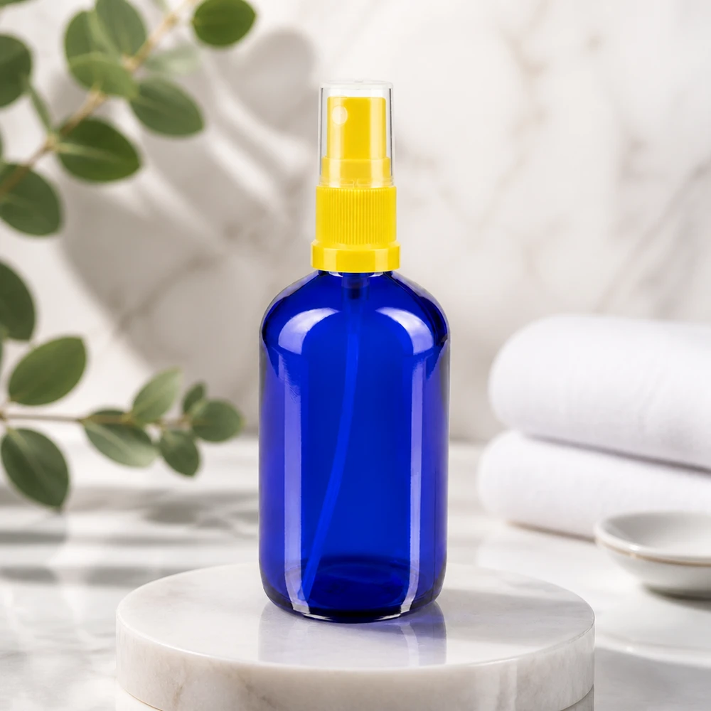 Flacon rond bleu de 100 ml en verre d'apothicaire, muni d'un vaporisateur à doigt jaune posé sur un socle en marbre