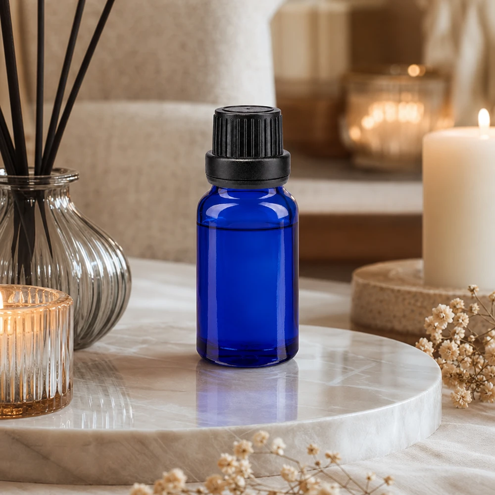 Petit flacon compte-gouttes bleu en verre anti-UV avec un insert de 2 mm, posé sur un plateau en marbre à côté de bougies