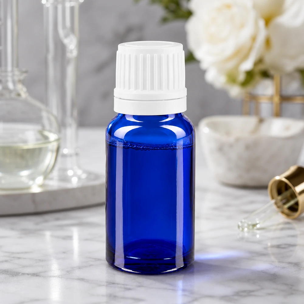 Flacon de pharmacie bleu 10ml bouchon inviolabilité blanc 1.2mm Flacon de pharmacie de 10 ml en verre bleu avec bouchon compte-gouttes blanc, posé sur une surface en marbre à côté de roses