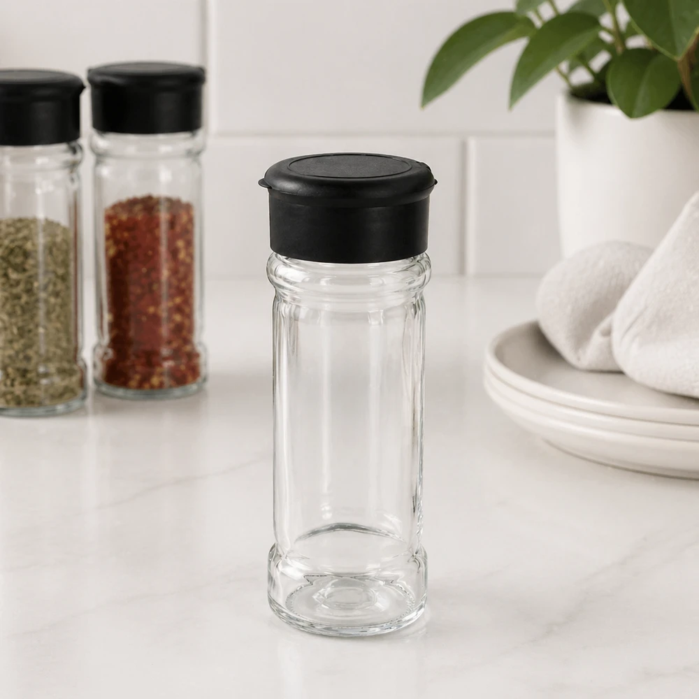 Petite salière en verre de 100 ml avec couvercle noir, posée sur un socle en marbre blanc