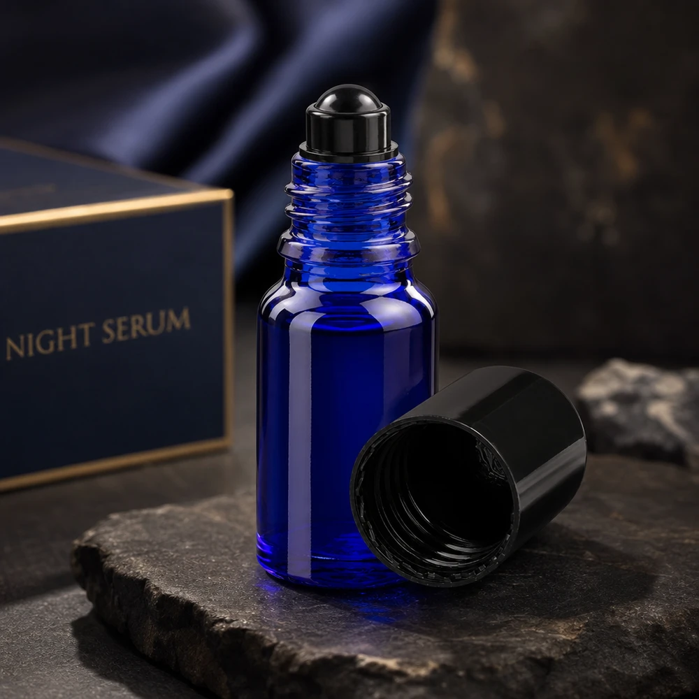 Flacon de déodorant en verre bleu 10 ml, déo à bille vide Flacon roll-on ApoGlas bleu foncé de 10 ml avec bouchon noir ouvert, posé sur une pierre d'ardoise devant un coffret de sérum de nuit