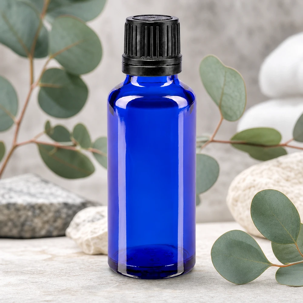 Bouteille de pharmacie bleue 30ml bouchon vissable noir bouchon d'inviolabilité Petite bouteille en verre bleue de 30 ml avec bouchon d'origine noir, devant des branches d'eucalyptus