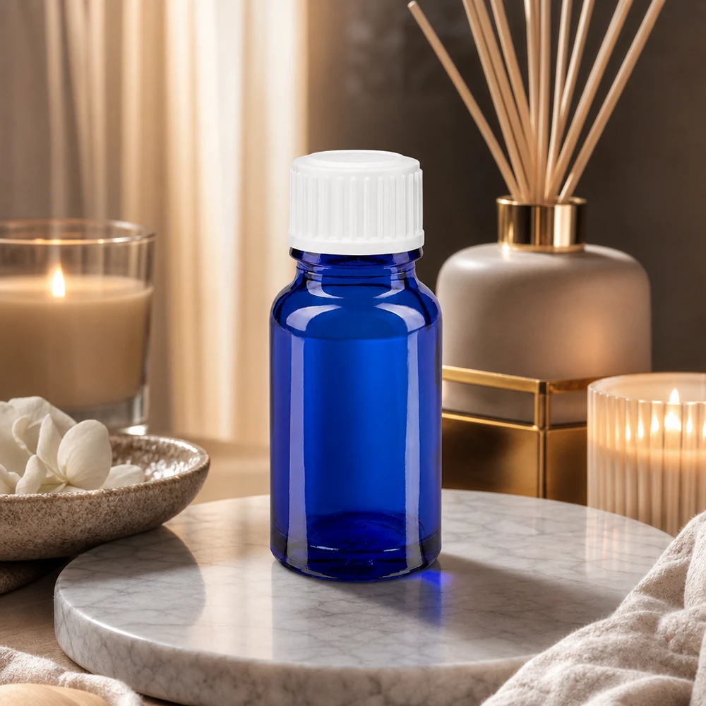 Flacon de pharmacie bleu 10ml bouchon vissable blanc standard Flacon en verre bleu de 10 ml avec un bouchon blanc, posé sur un plateau en marbre et entouré de bougies et d'un parfum d'ambiance