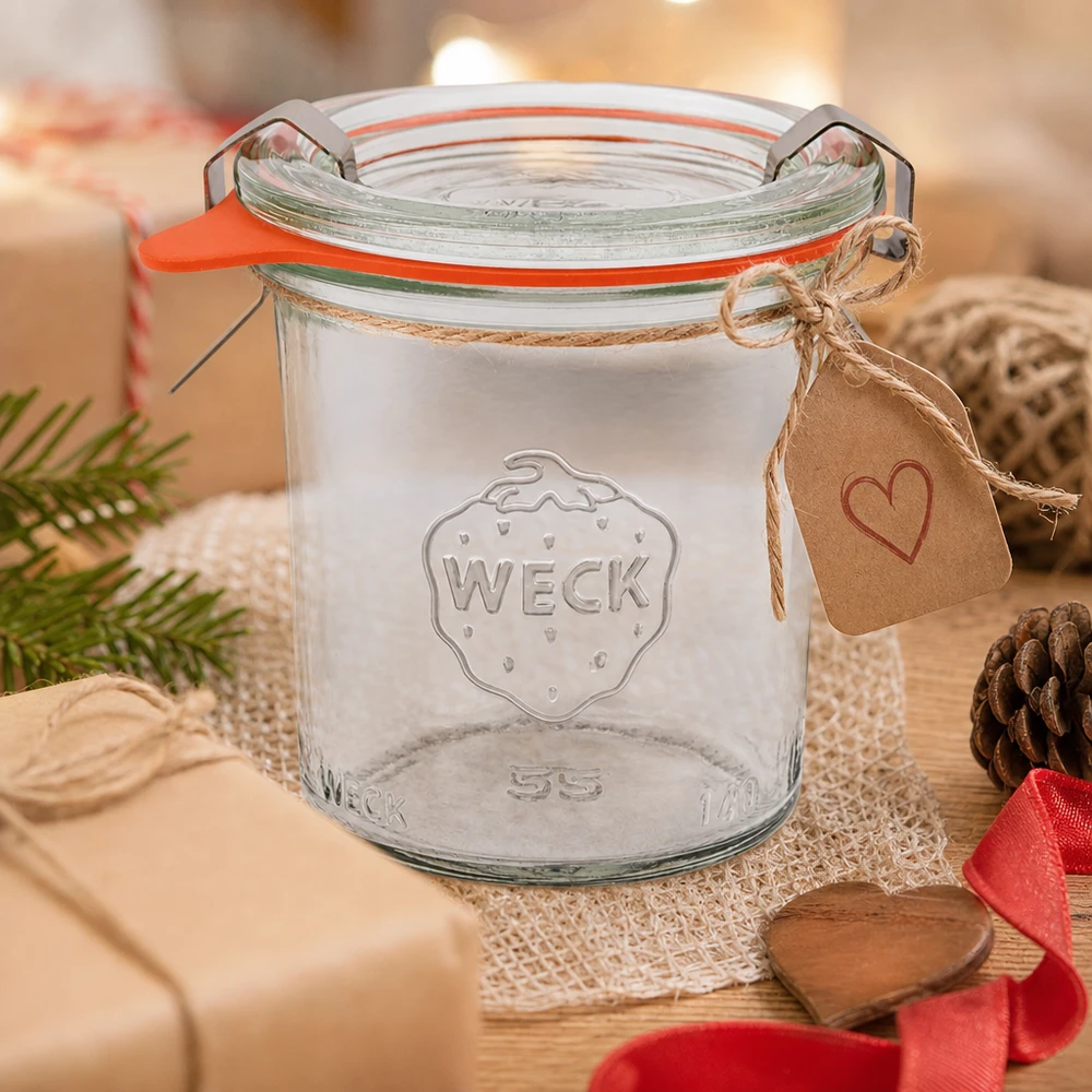 WECK Verre renversé 140ml RR60 comme idée de cadeau décoré avec un pendentif en forme de cœur et une corde de jute sur une table en bois avec des pommes de pin