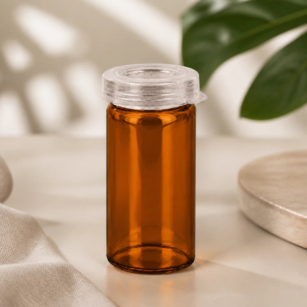 Tube à comprimés en verre couleur ambre de 5 ml avec un bouchon à encliqueter en plastique transparent, sur fond clair
